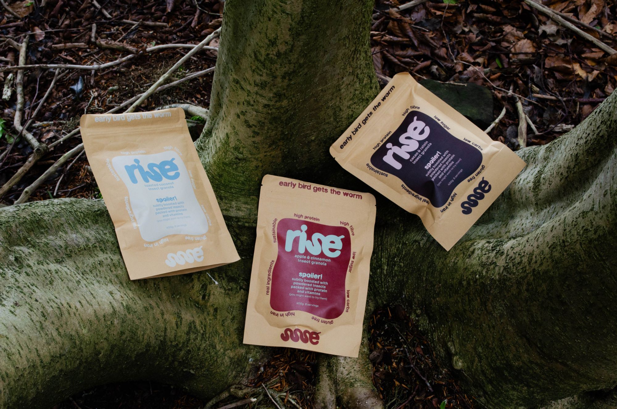 Three rise insect granola pouches resting on a mossy tree root